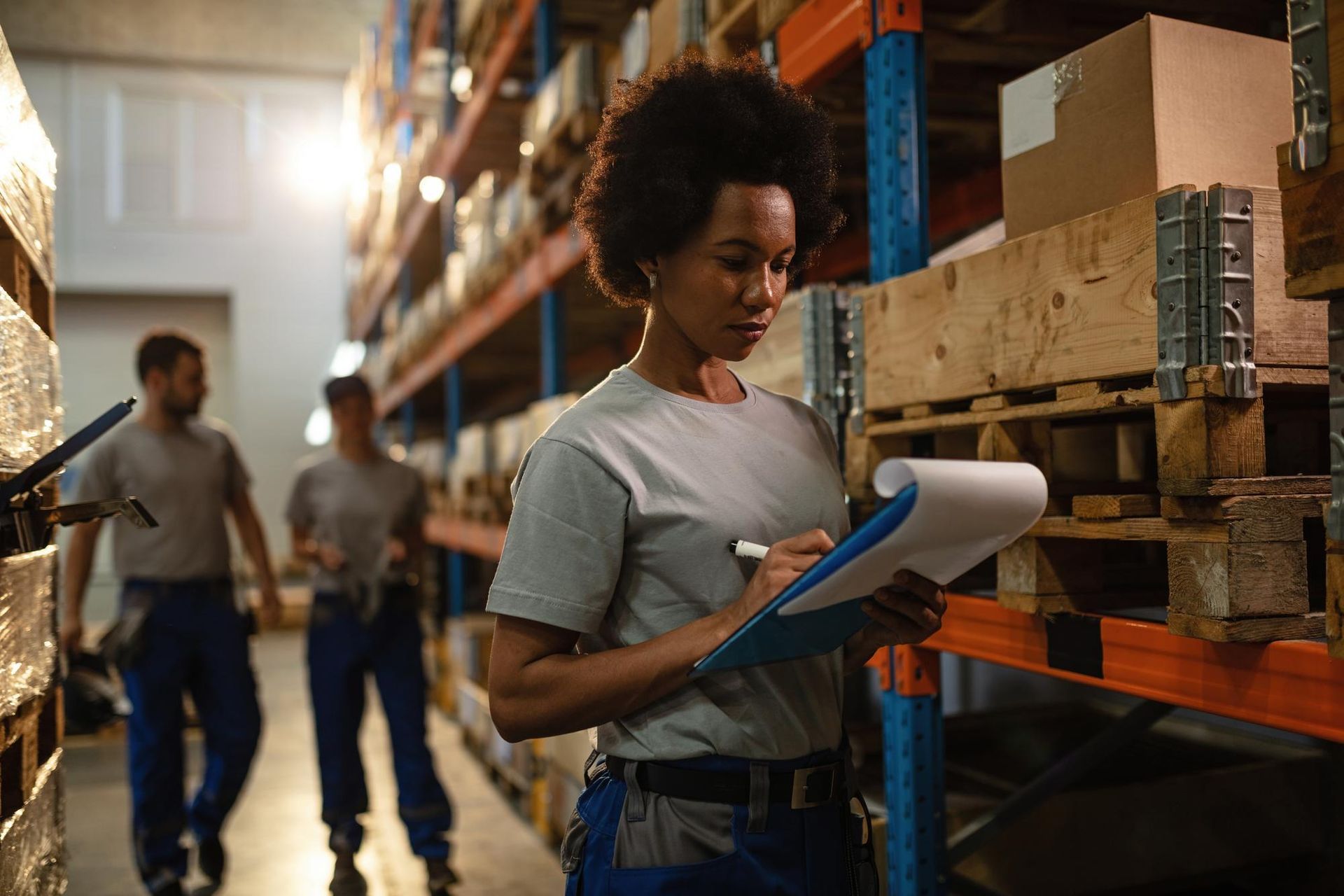 A woman is writing on a clipboard in a warehouse.