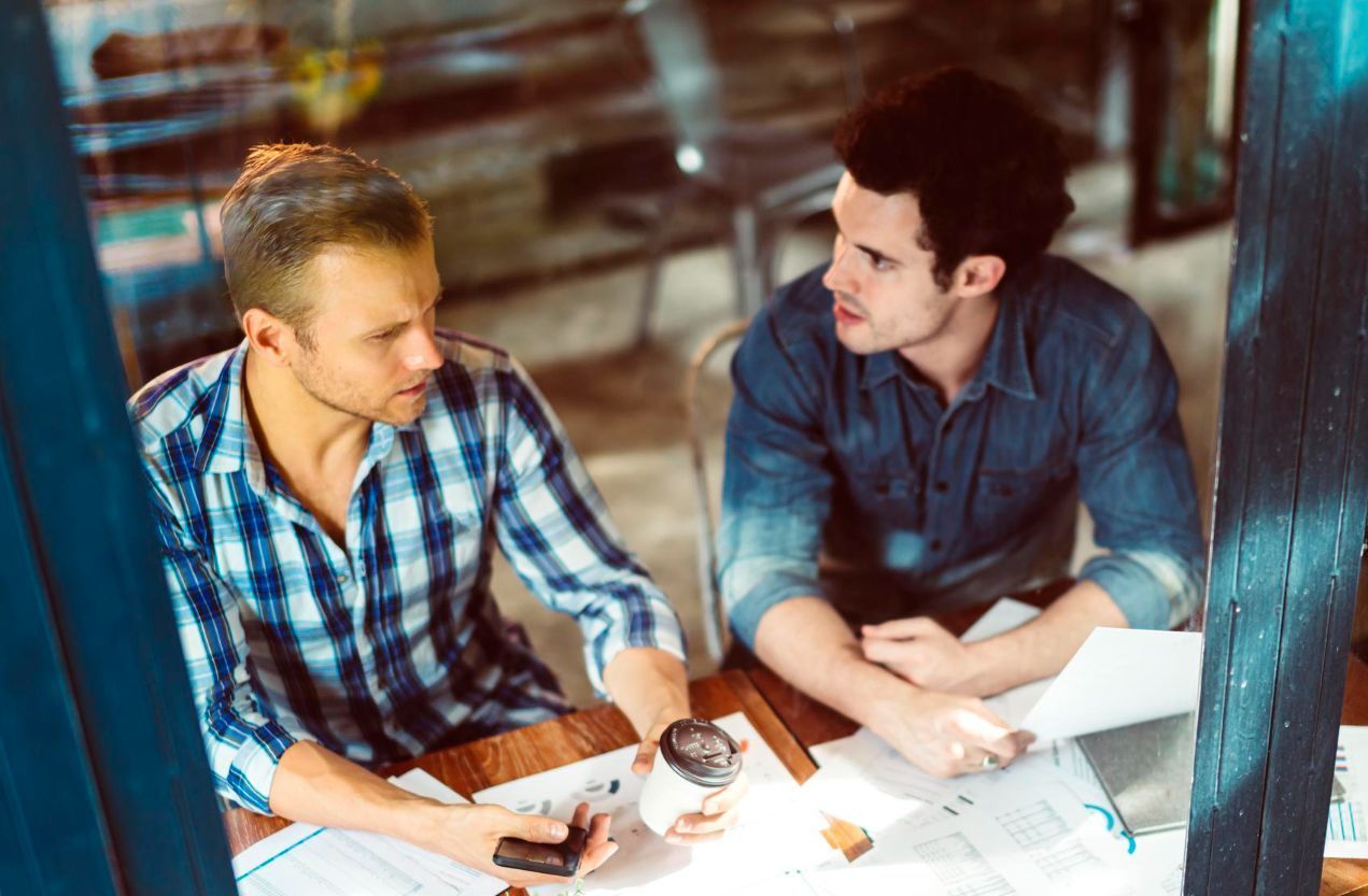Two men are sitting at a table talking to each other.