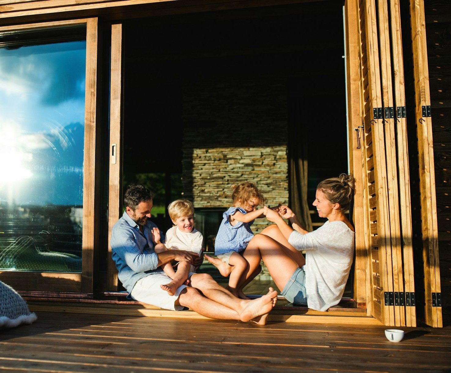 A family is sitting on a wooden deck in front of a window.