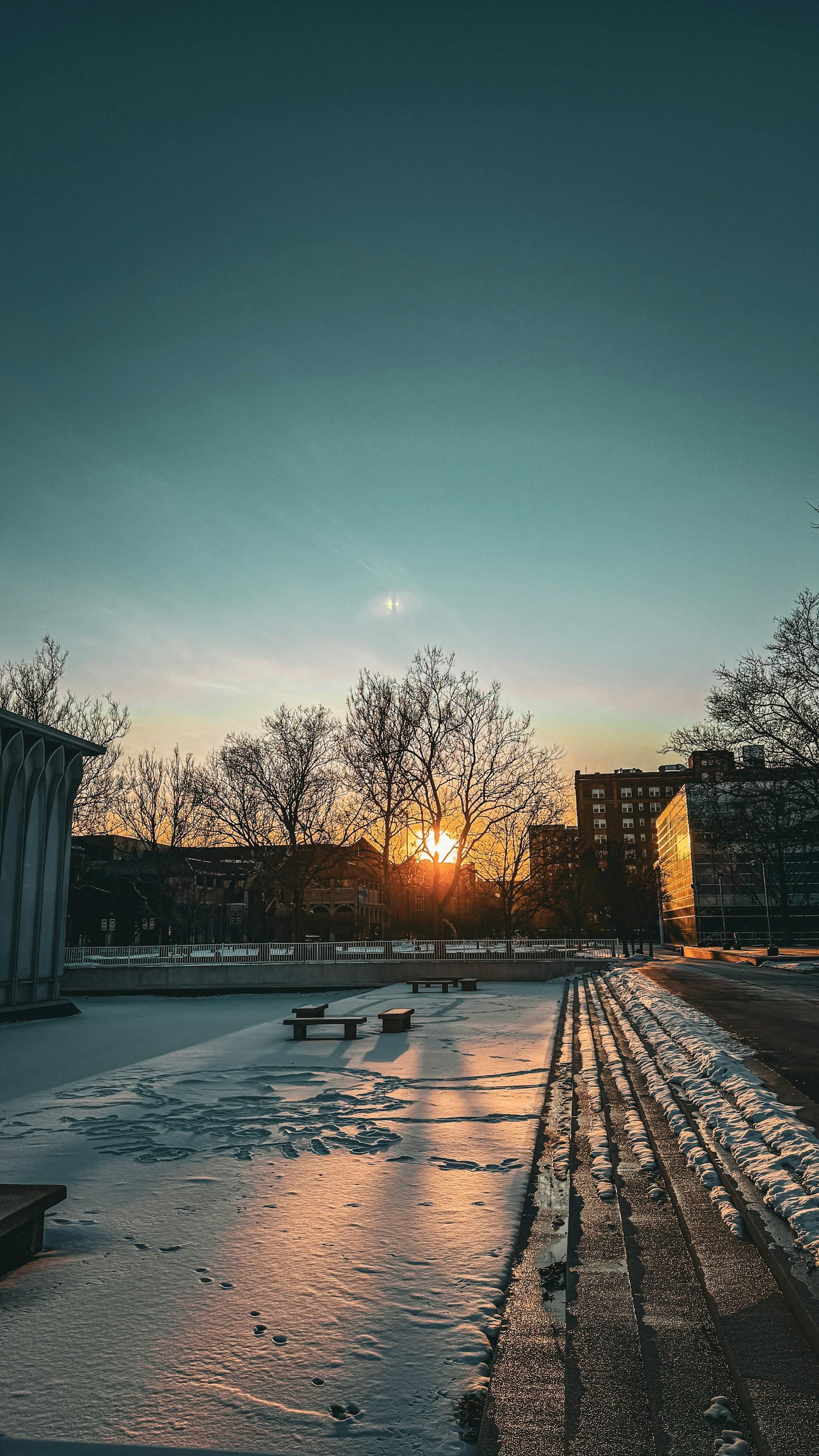 The sun is setting over a frozen lake in a city.