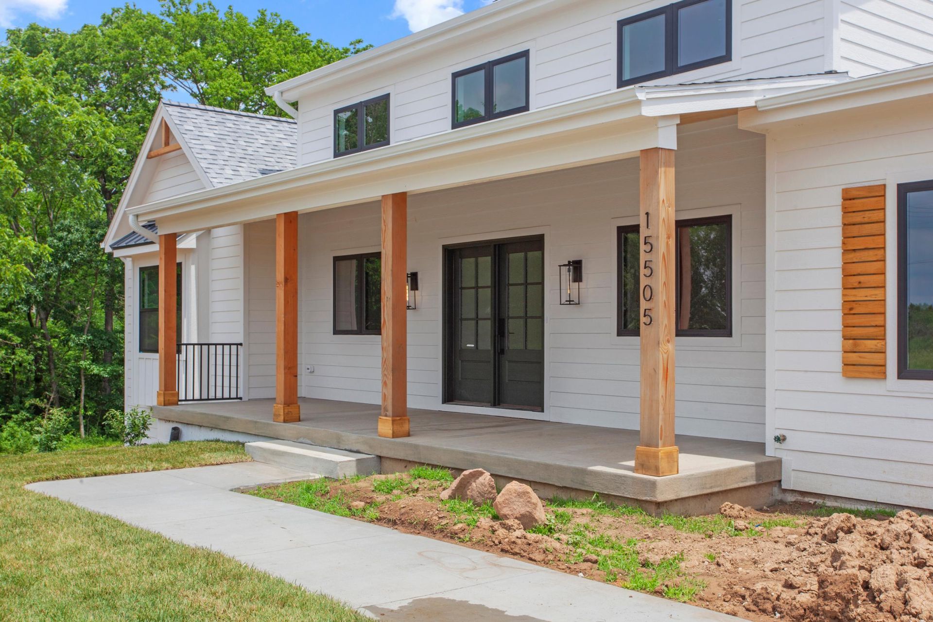 White house with black trim and wooden porch columns, on a sunny day.