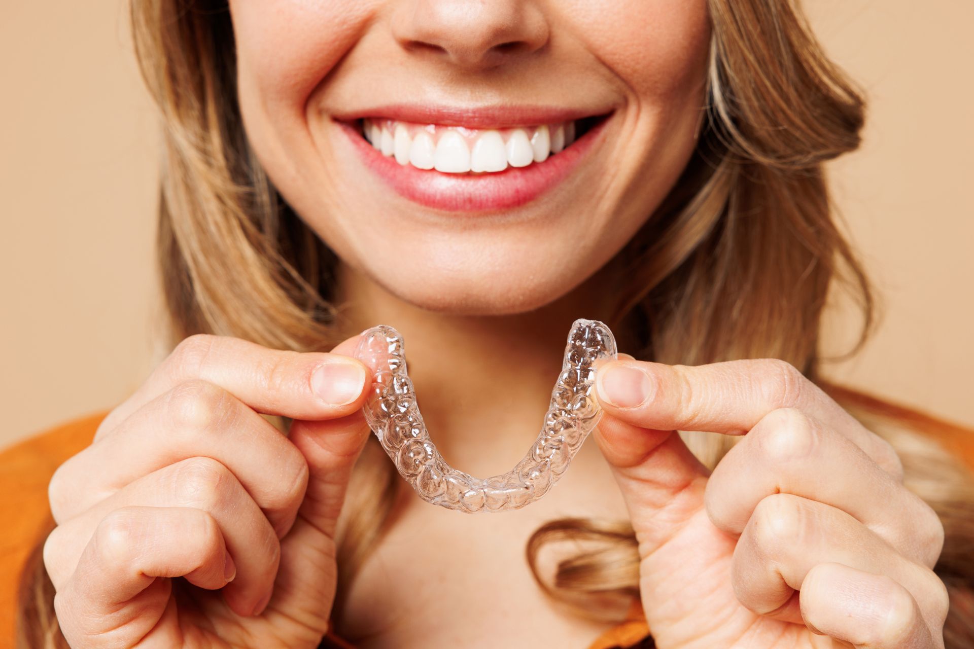 Person holding a clear Invisalign aligner while showing a bright, straight smile. Person holding a clear Invisalign aligner while showing a bright, straight smile.