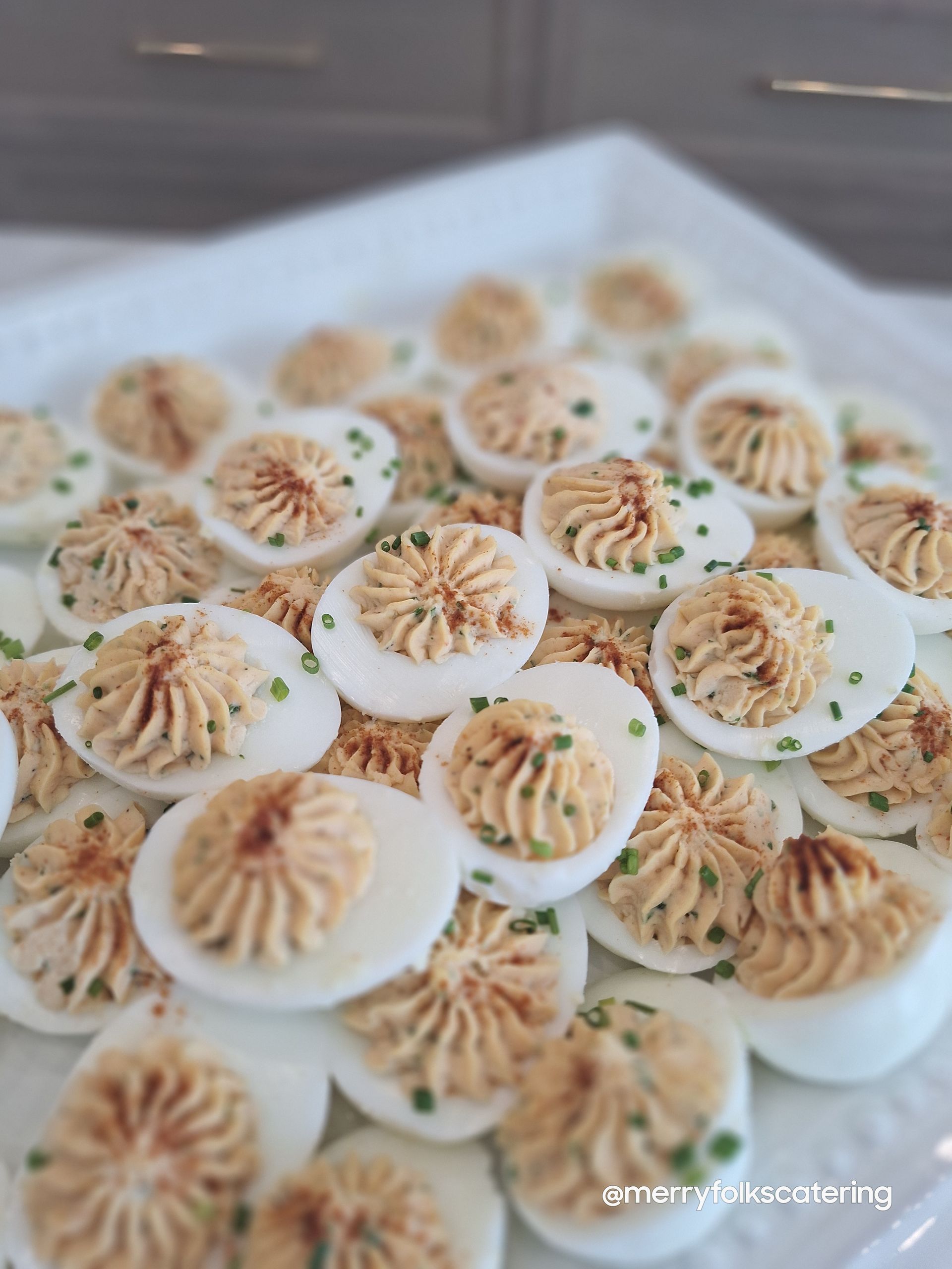 Deviled eggs arranged on a white platter, topped with a creamy filling and sprinkled with chives.