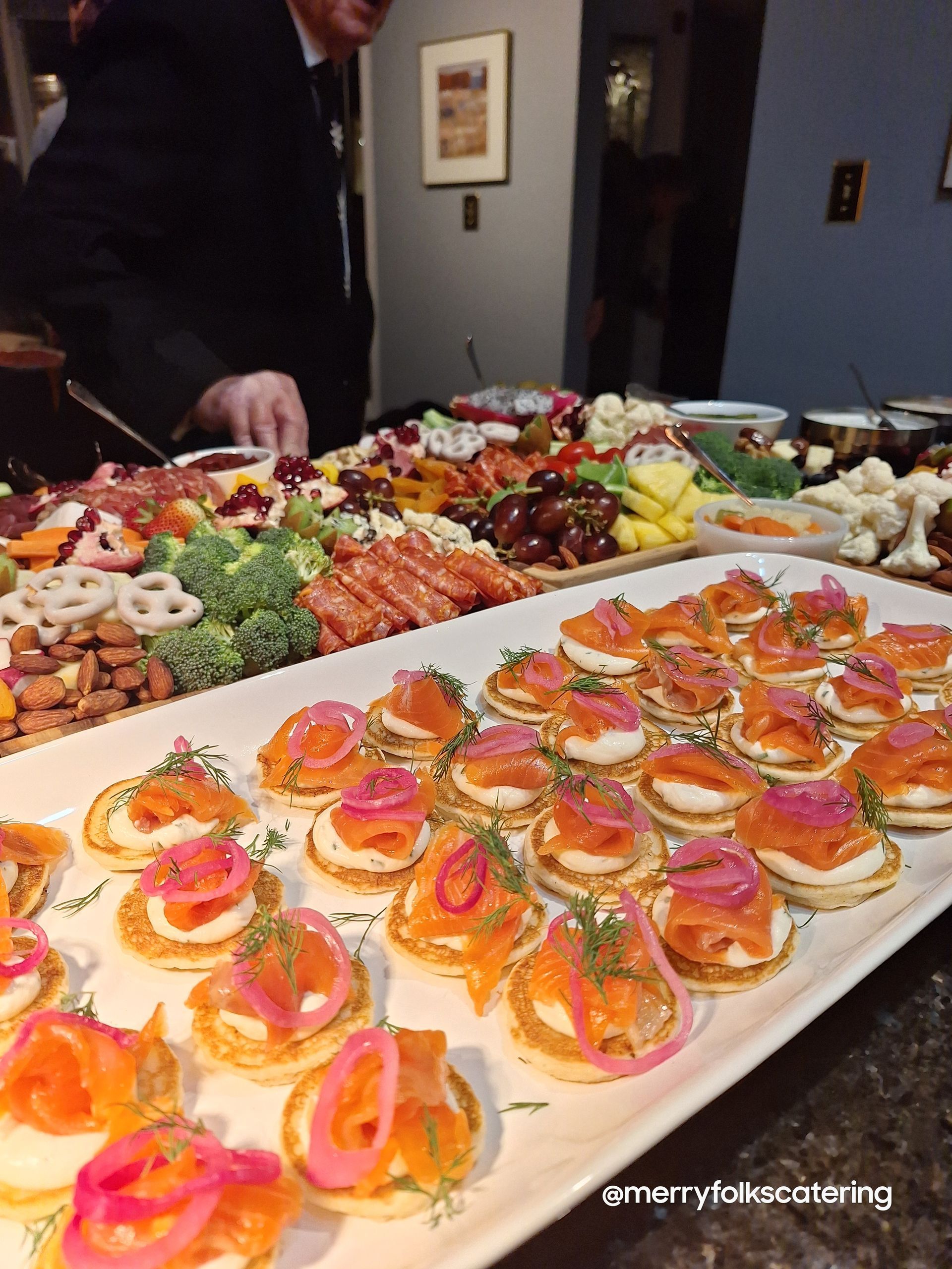 Tray of appetizers featuring salmon, onions, and dill; other food platters in background.