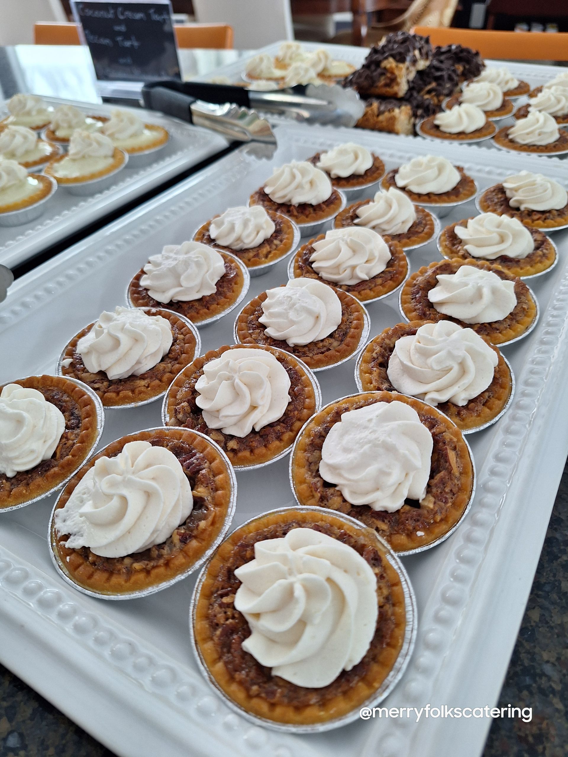 A tray of mini pecan pies topped with whipped cream, ready for serving.