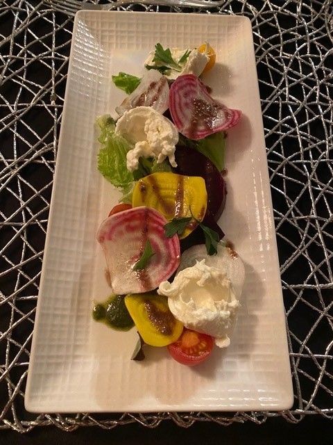 Beet salad with colorful beets, cheese, and dressing on a white rectangular plate.