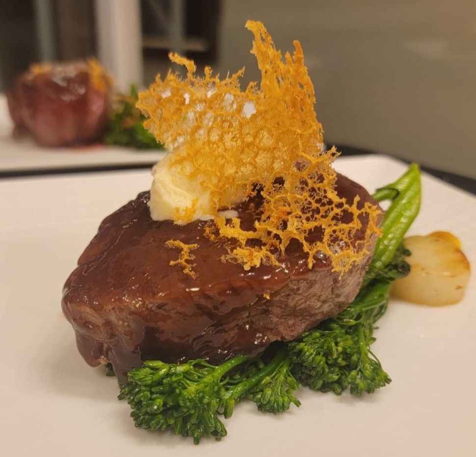 Seared steak on broccoli with cheese crisp, white plate, and a blurred onion.