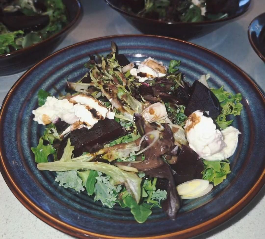 Salad with dark beets, white cheese, greens, and balsamic glaze in a blue bowl.