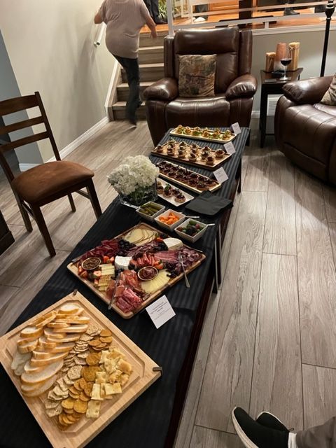 Charcuterie spread on a table; person walks up stairs. Cheese, crackers, meats, appetizers.
