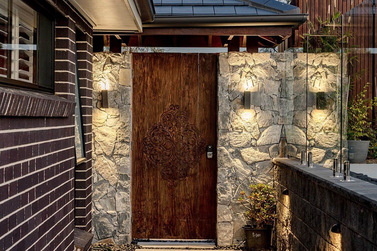 Stone path leads to a pool in a sunny backyard with lush green trees and blue sky.