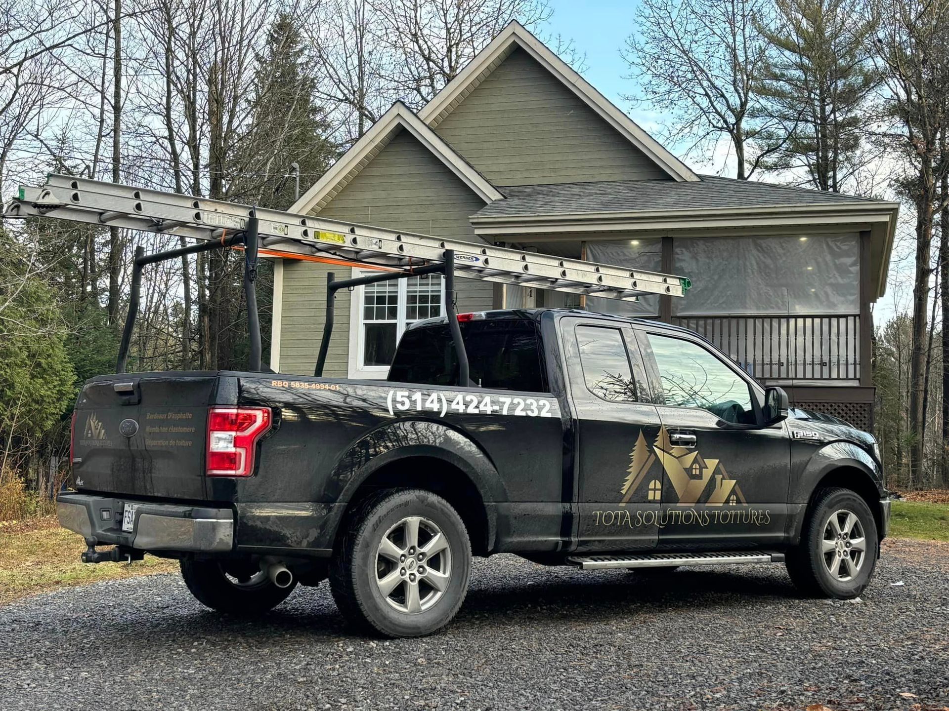 Un camion noir avec un porte-échelle à l'arrière est garé devant une maison.