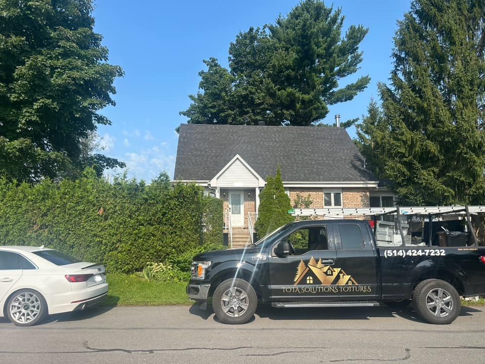 Un camion noir avec le logo d'une entreprise de toiture est garé devant une maison