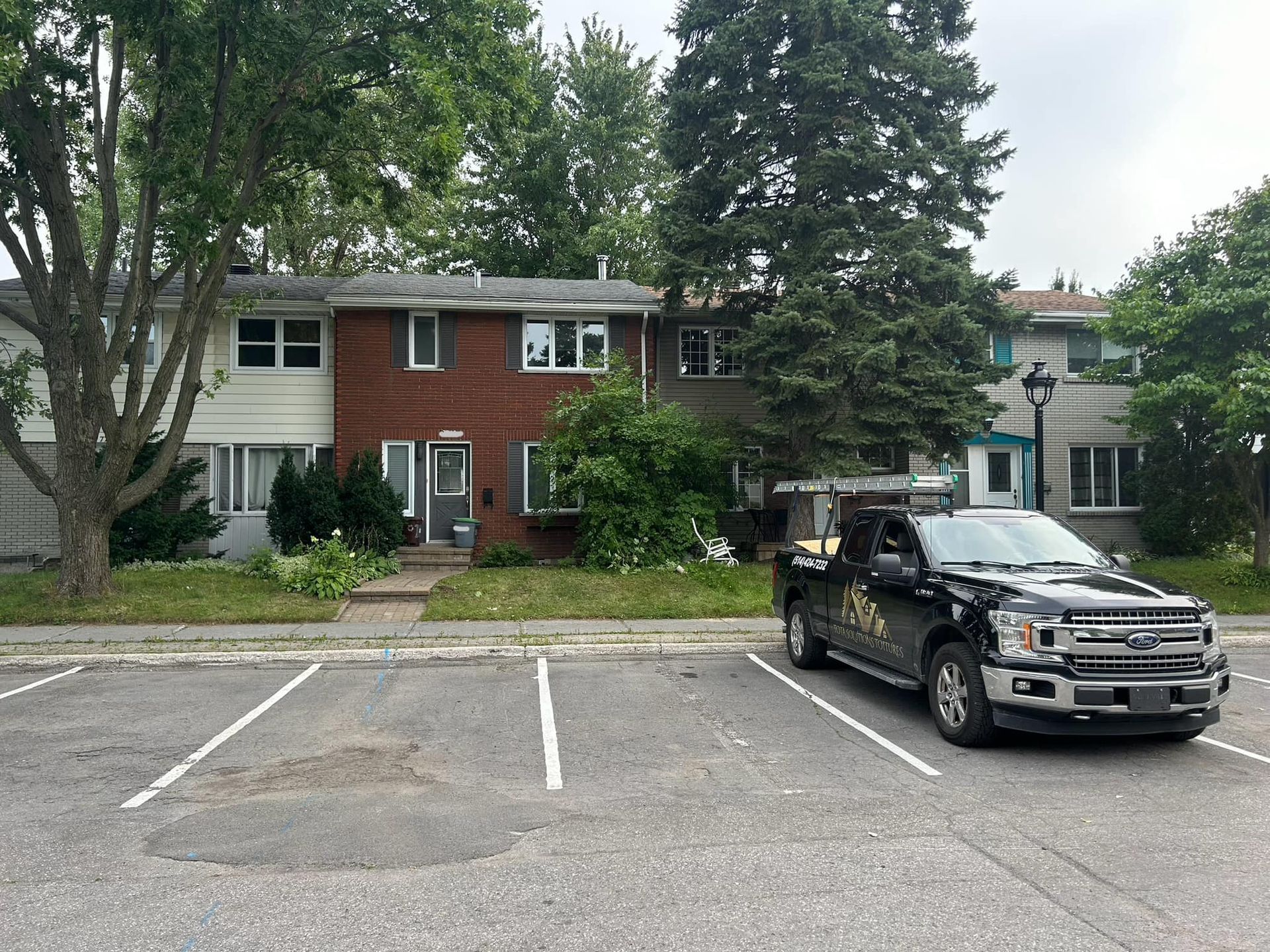 Un camion noir est garé sur un parking devant une maison.