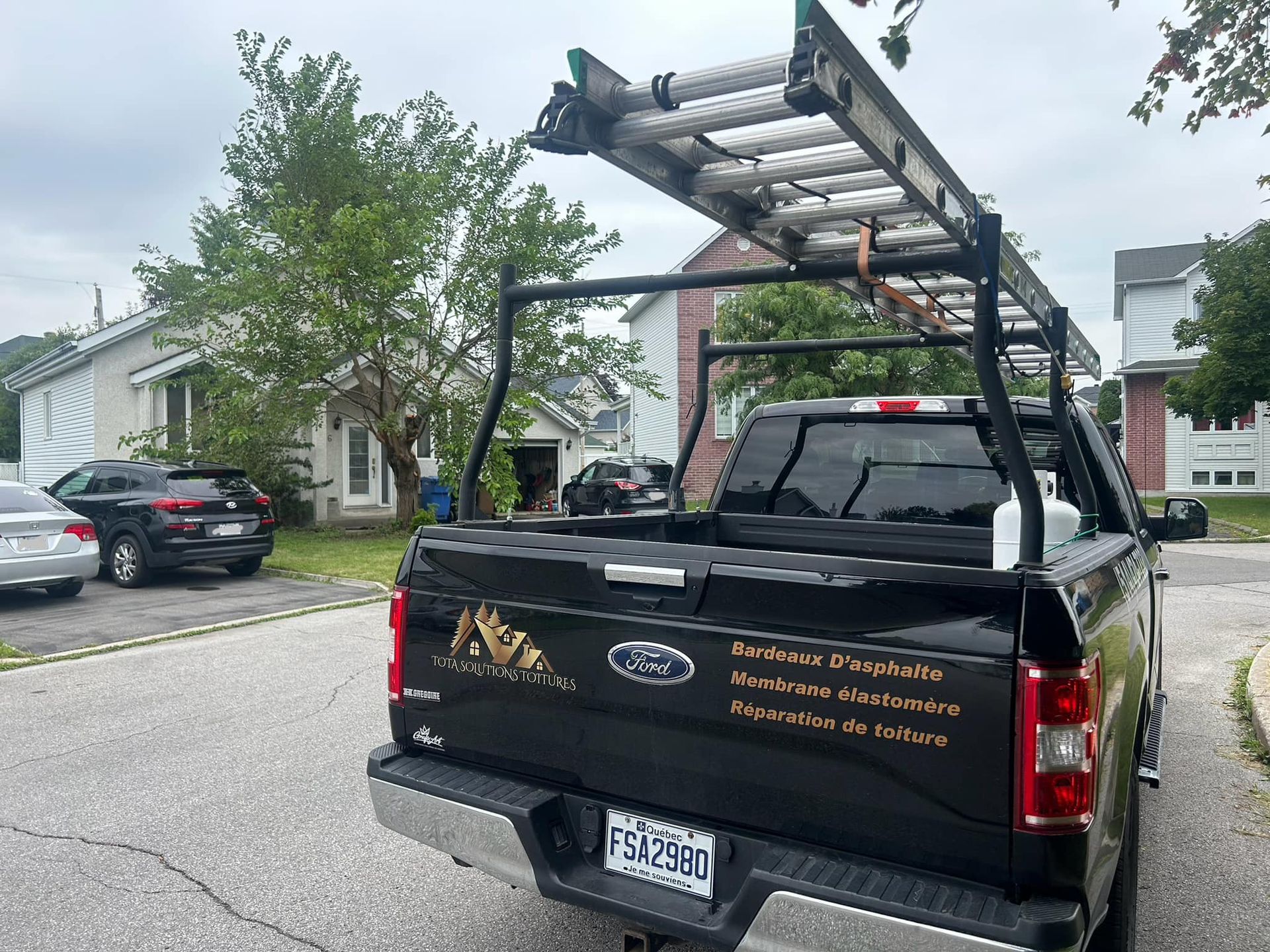 Un camion noir avec un porte-échelle à l'arrière est garé sur le bord de la route.
