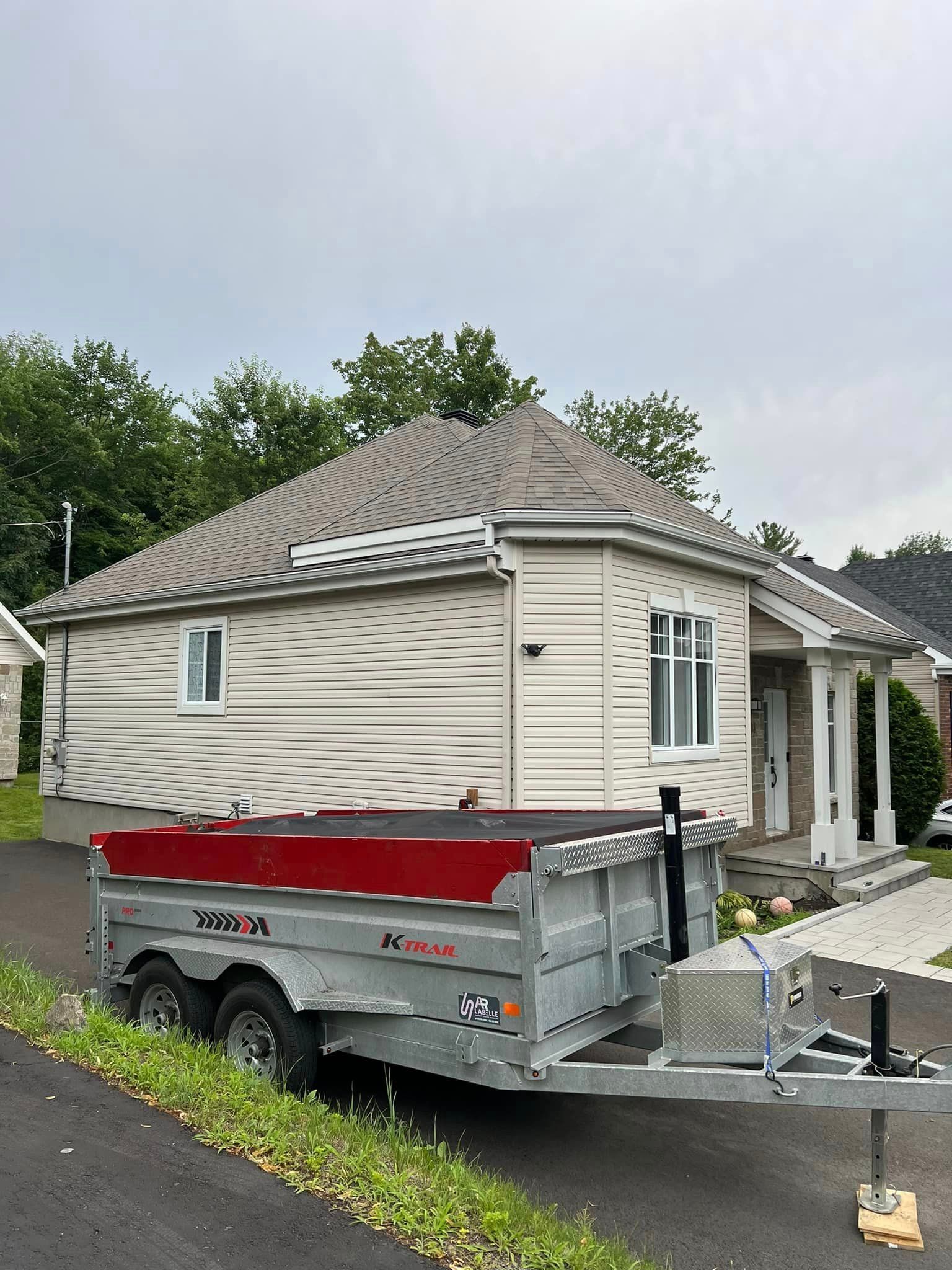 Une remorque est garée devant une petite maison blanche.