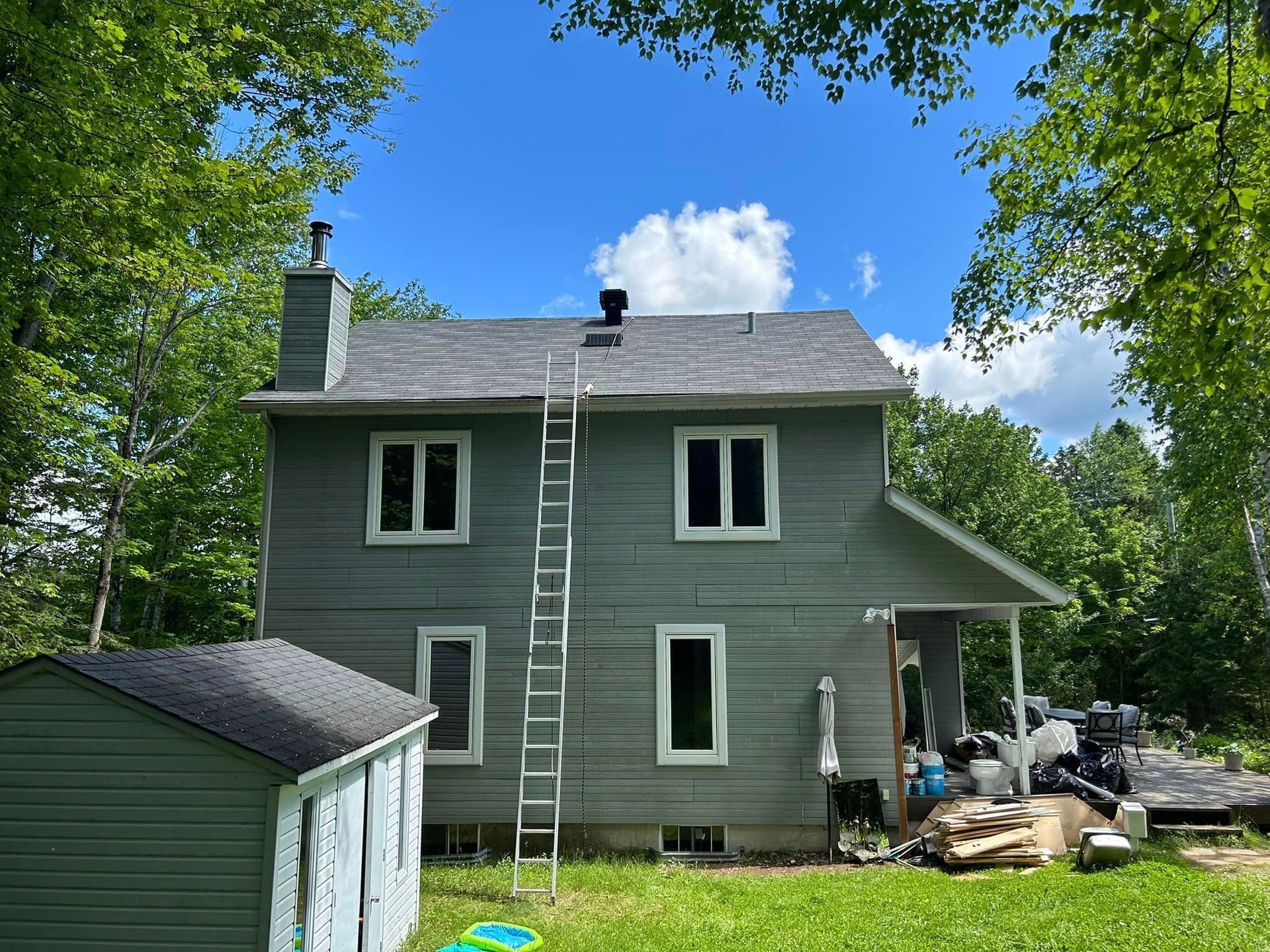 Une maison avec une échelle sur le toit et un hangar dans la cour arrière.