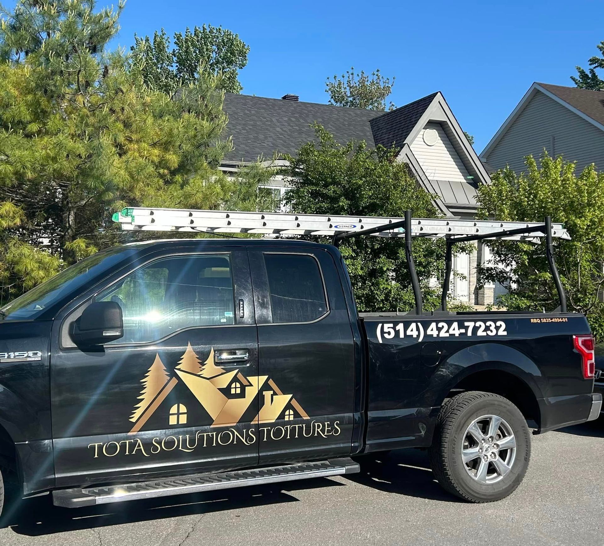 Un camion noir portant l'inscription Total Solutions Roofing est garé devant une maison