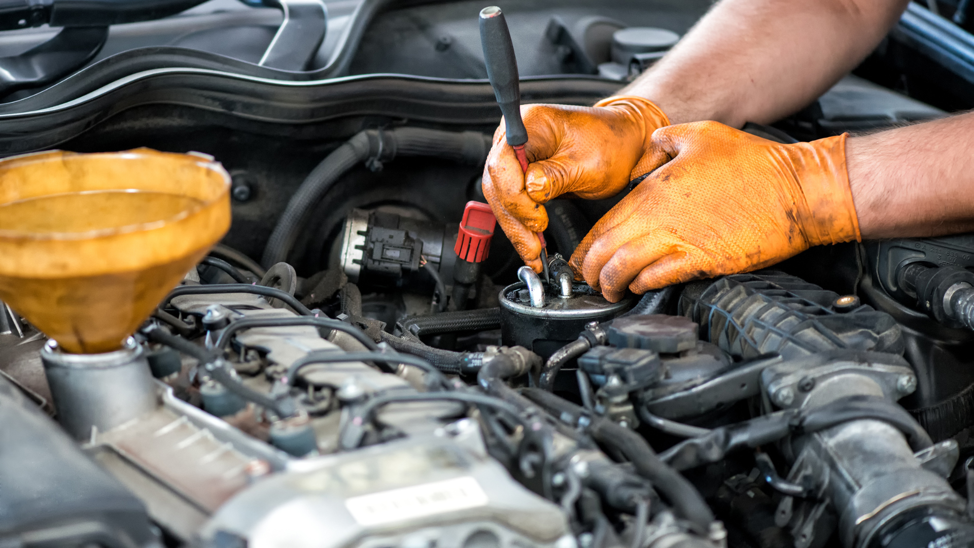A man wearing orange gloves is working on a car engine.
