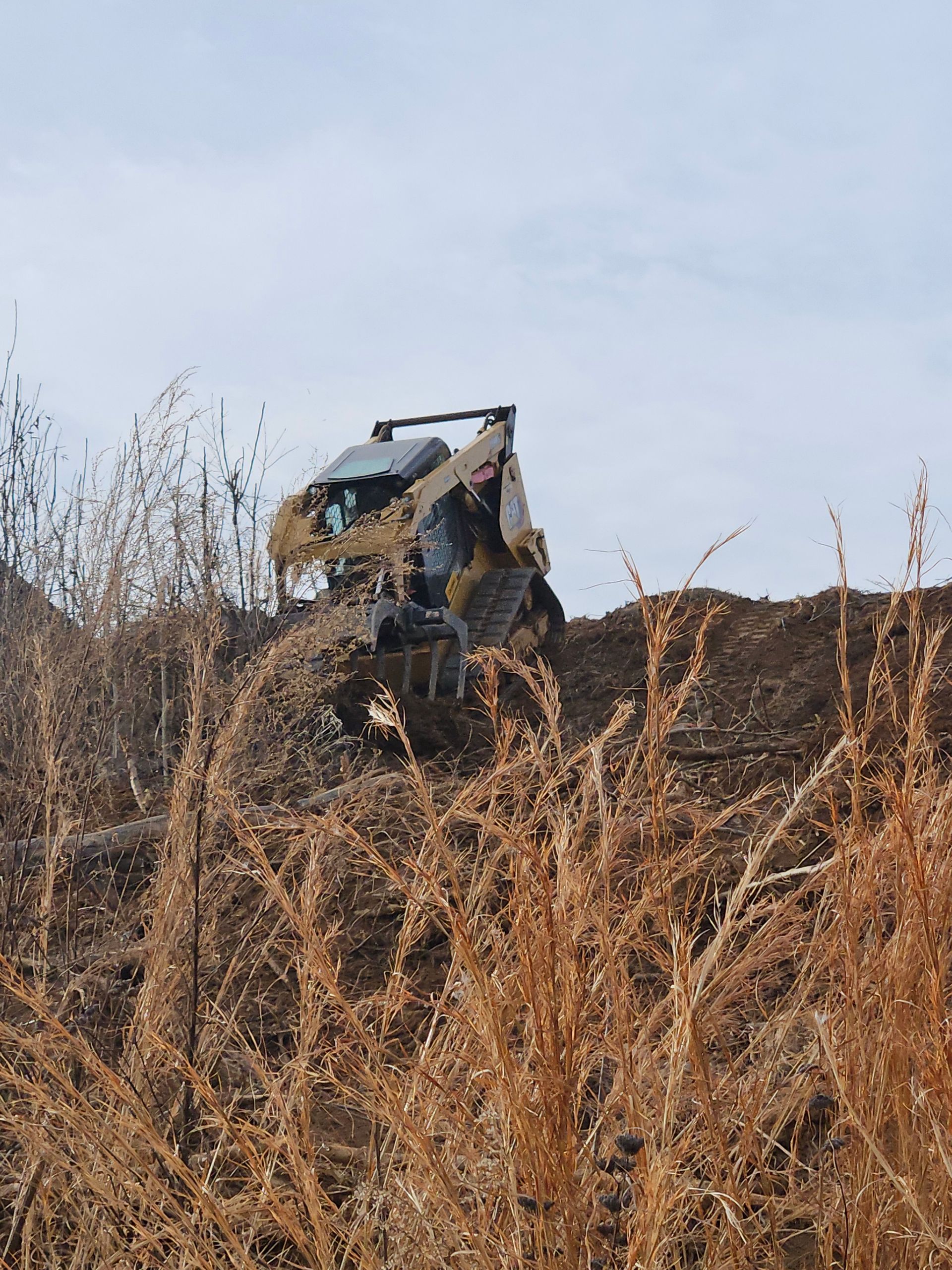 A bulldozer is driving down a hill in a field of dry grass.