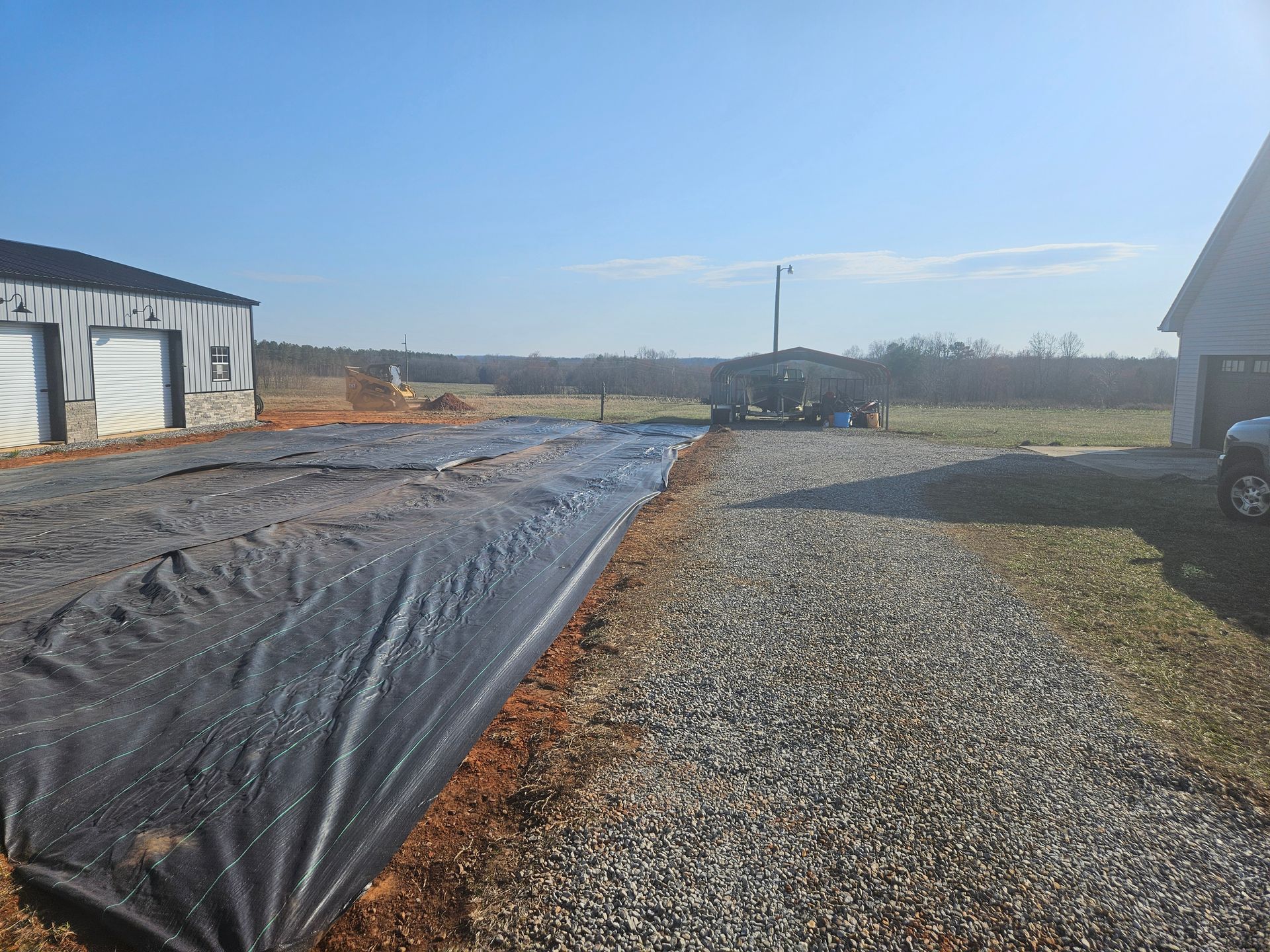 A black tarp is covering a gravel road in front of a garage.