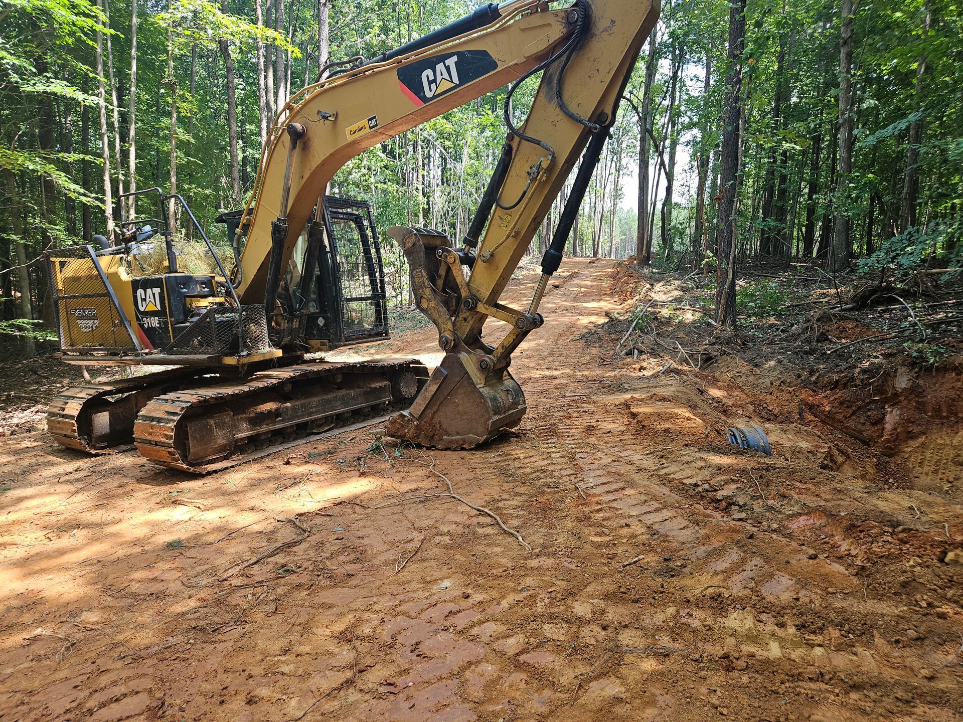 A cat excavator is sitting on the side of a dirt road in the woods.