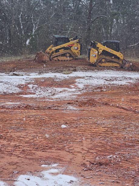 Two bulldozers are working on a dirt field in the snow.