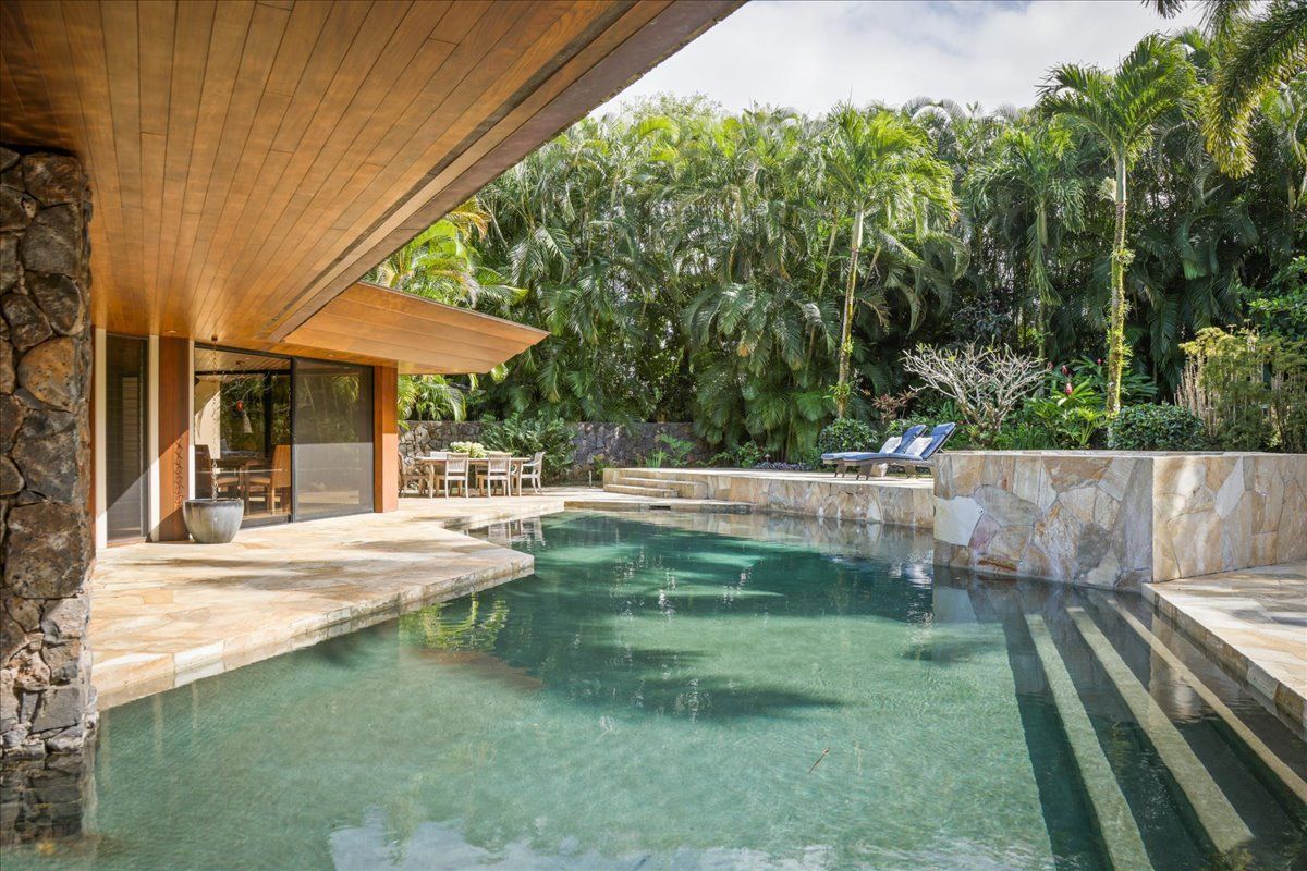 A large swimming pool in the backyard of a house surrounded by trees.