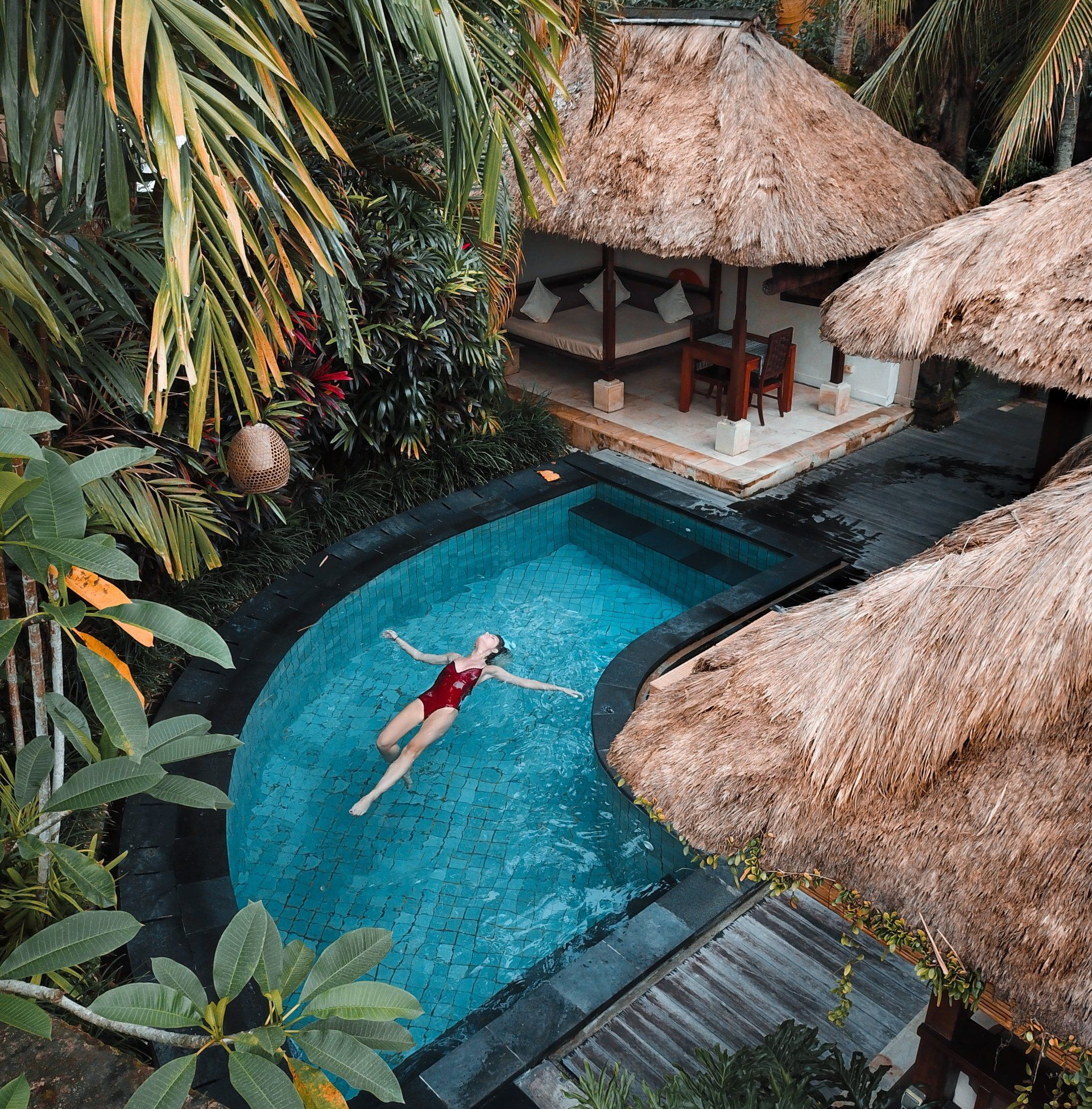 A woman is floating on her back in a swimming pool surrounded by palm trees.