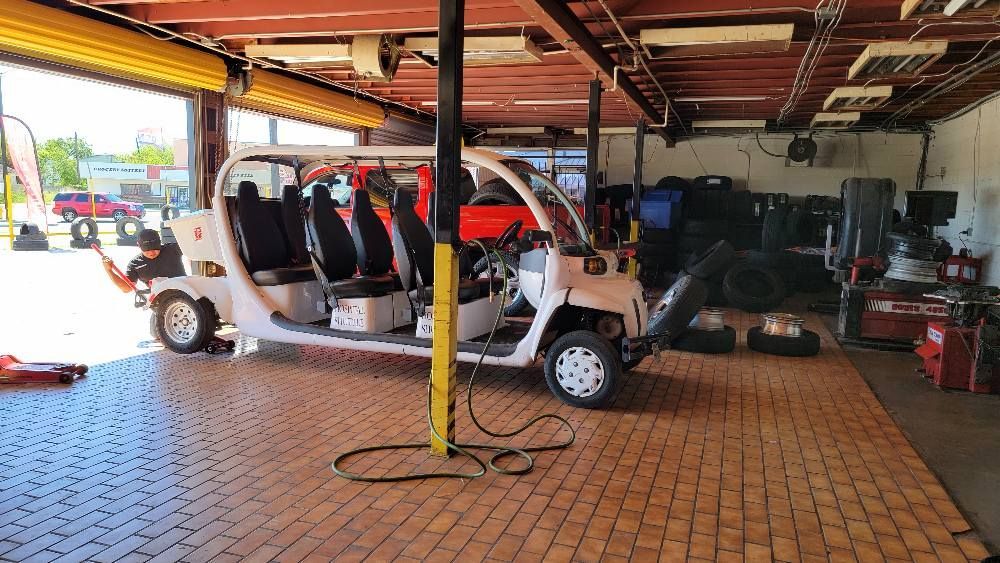 White multi-seat vehicle in a repair bay with tools and tires visible. Open garage door.