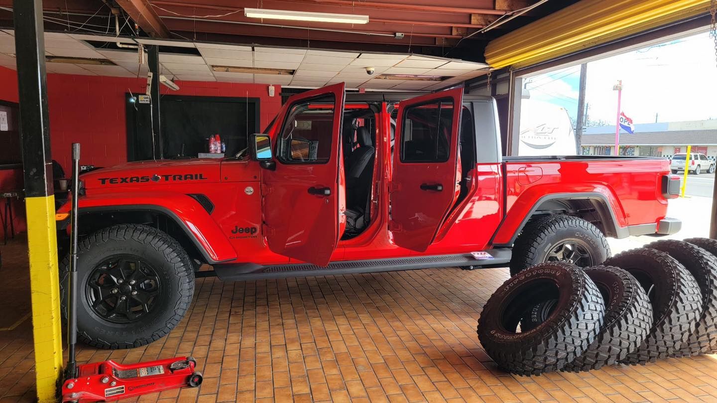 Red Jeep Gladiator with open doors inside a shop, tires in front.