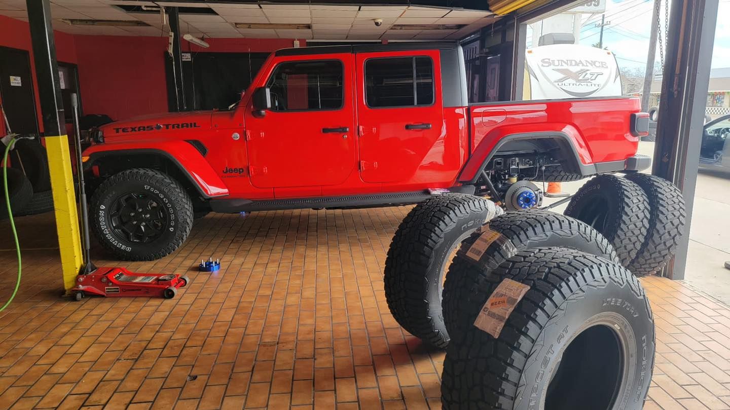 Red Jeep Gladiator pickup truck in a shop, tires in front.