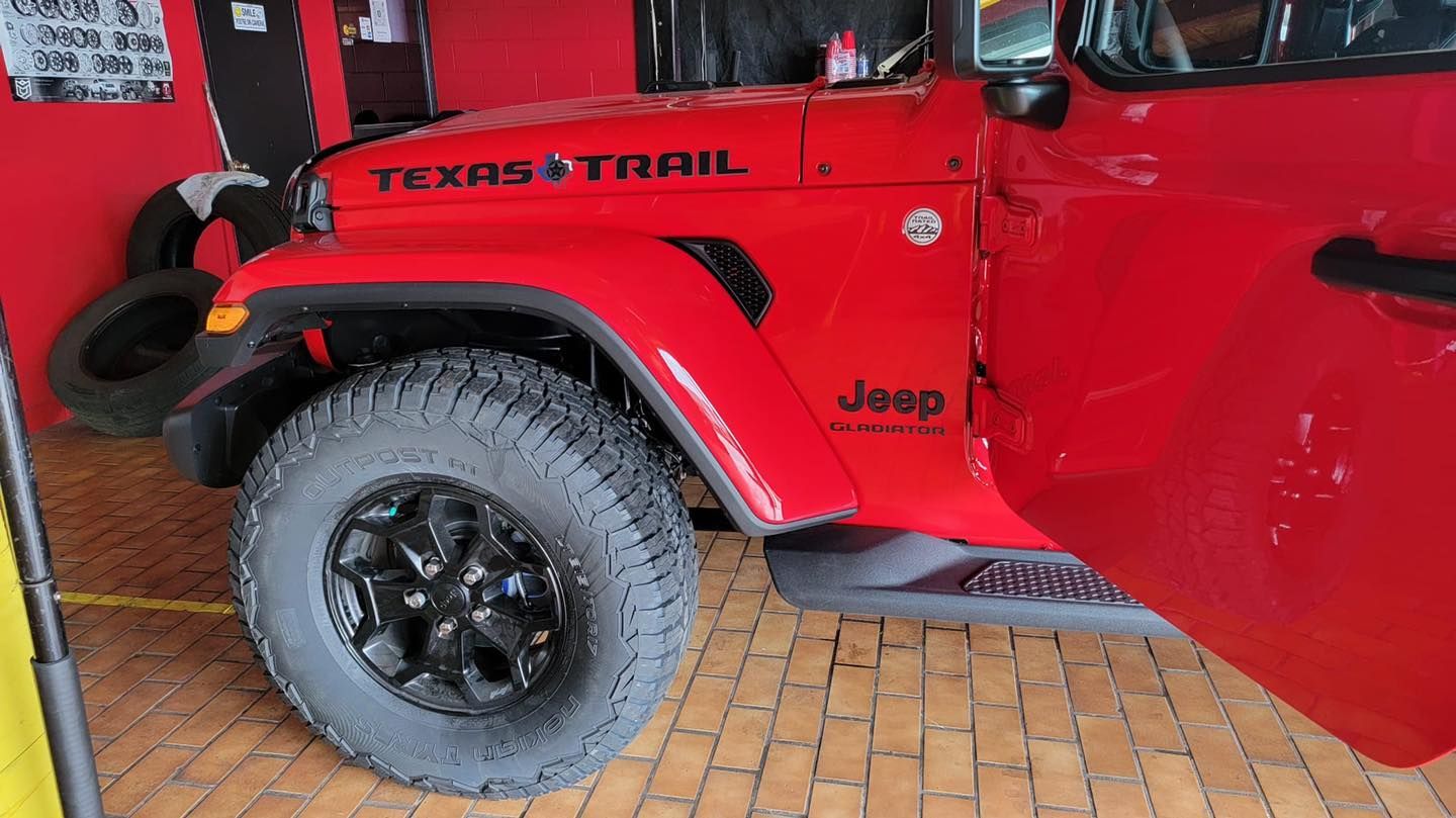 Red Jeep Texas Trail with black wheels and open door.