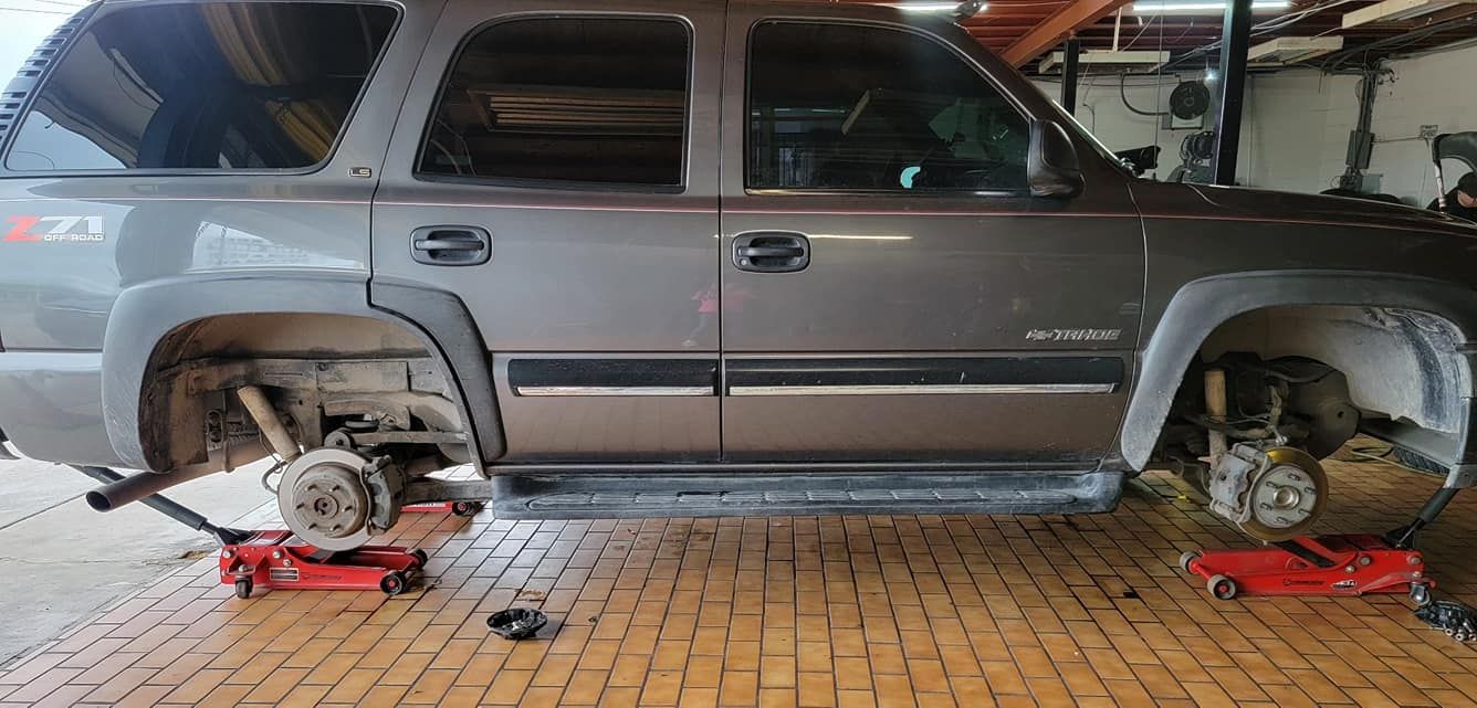 Gray SUV on red jacks with wheels removed, in a garage setting.