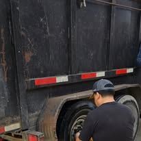 Person in black shirt fixing a tire on a black trailer with red and white reflective stripes.