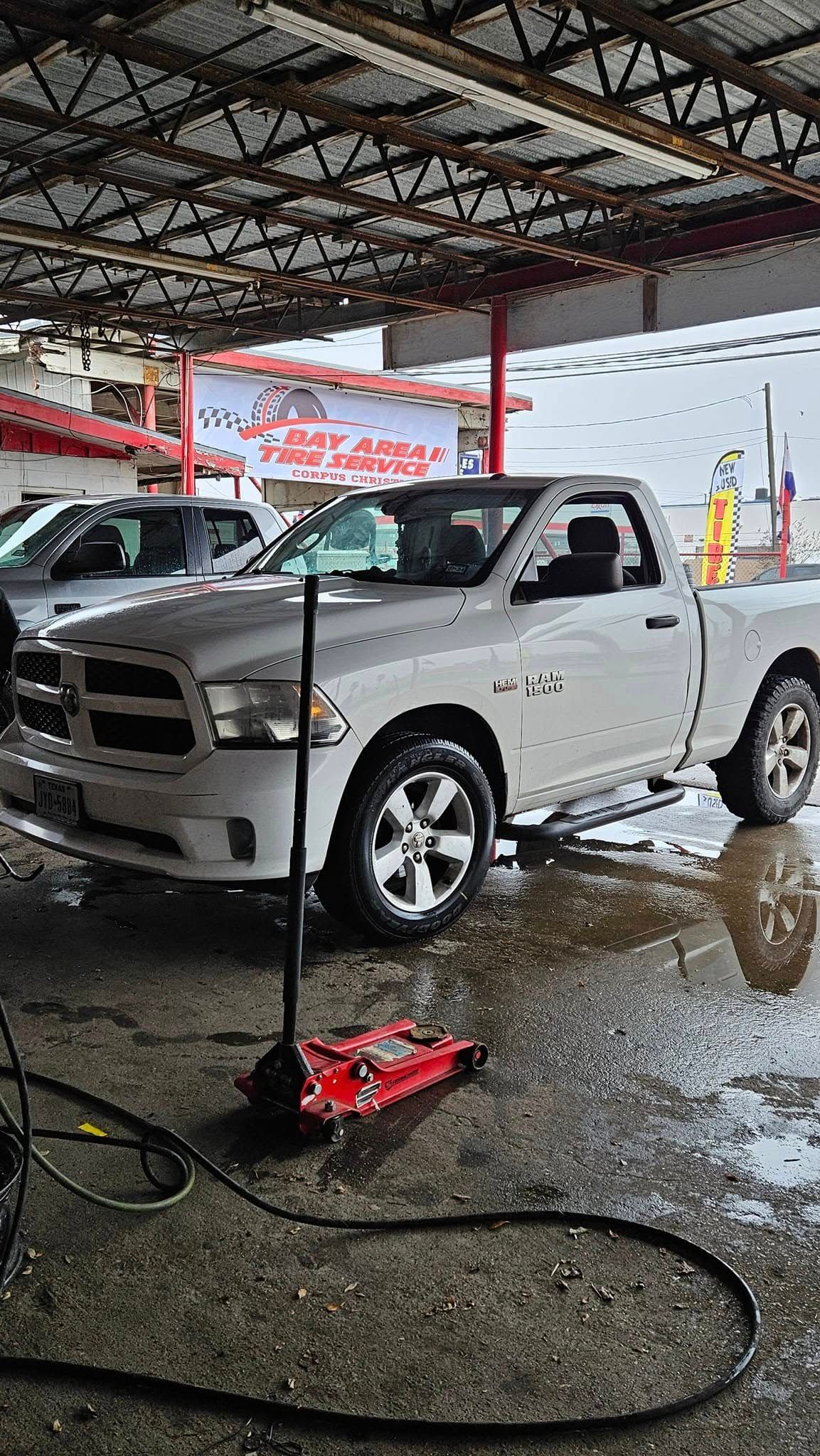 White Dodge Ram pickup truck at a car wash, with black hose and red jack on the wet ground.