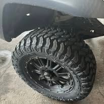 Close-up of a black truck tire with a deep tread pattern, mounted on a black rim.