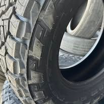 Close-up of a black tire with a rugged tread pattern, next to a stack of other tires.