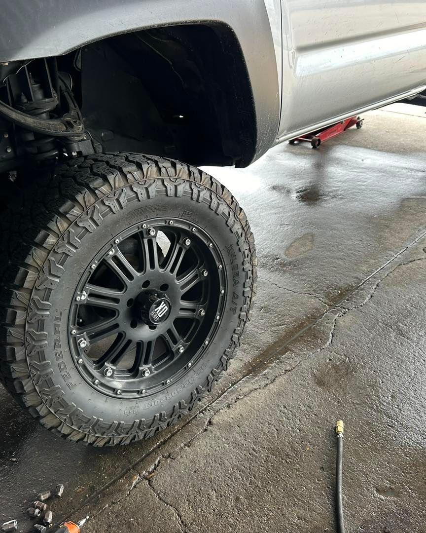 Black tire on a truck with black rims in a garage setting.
