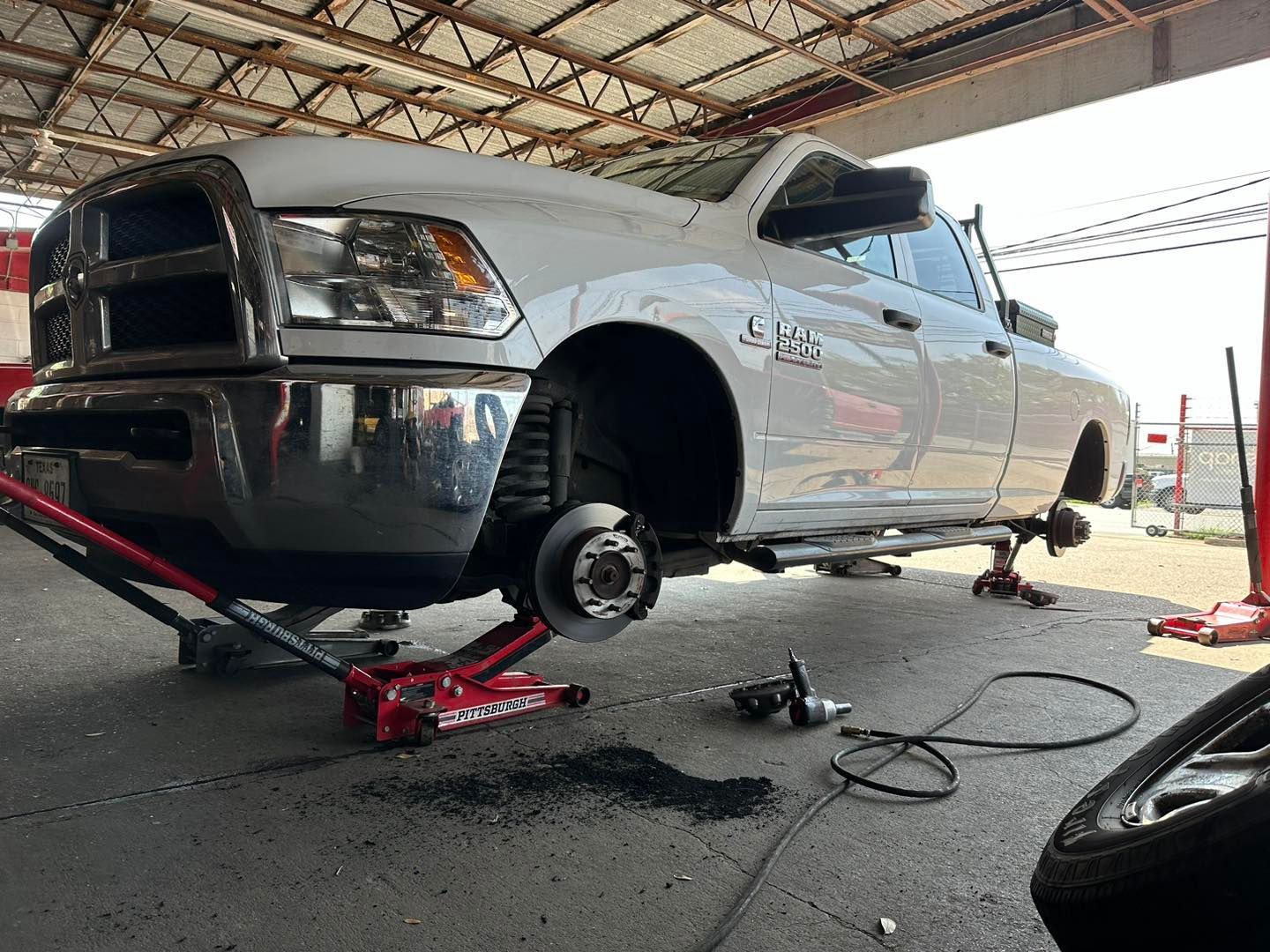 White pickup truck raised on jacks at a repair shop, tire removed, tools nearby.
