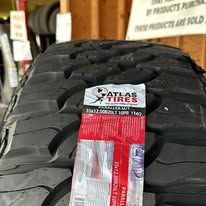 Close-up of a black Atlas tire. The tread is deep and the tire has a red and white label attached.
