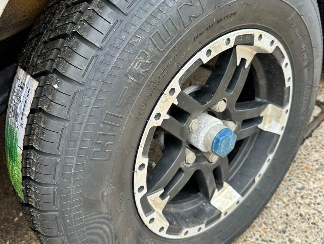 Close-up of a trailer tire and wheel. The tire is black with some writing, and the wheel is black and silver.