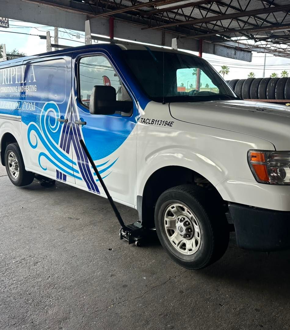 White and blue van with logo being jacked up inside a garage, next to a stack of tires.