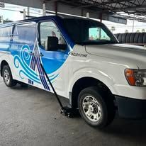 White and blue van with logo parked; jack in place.