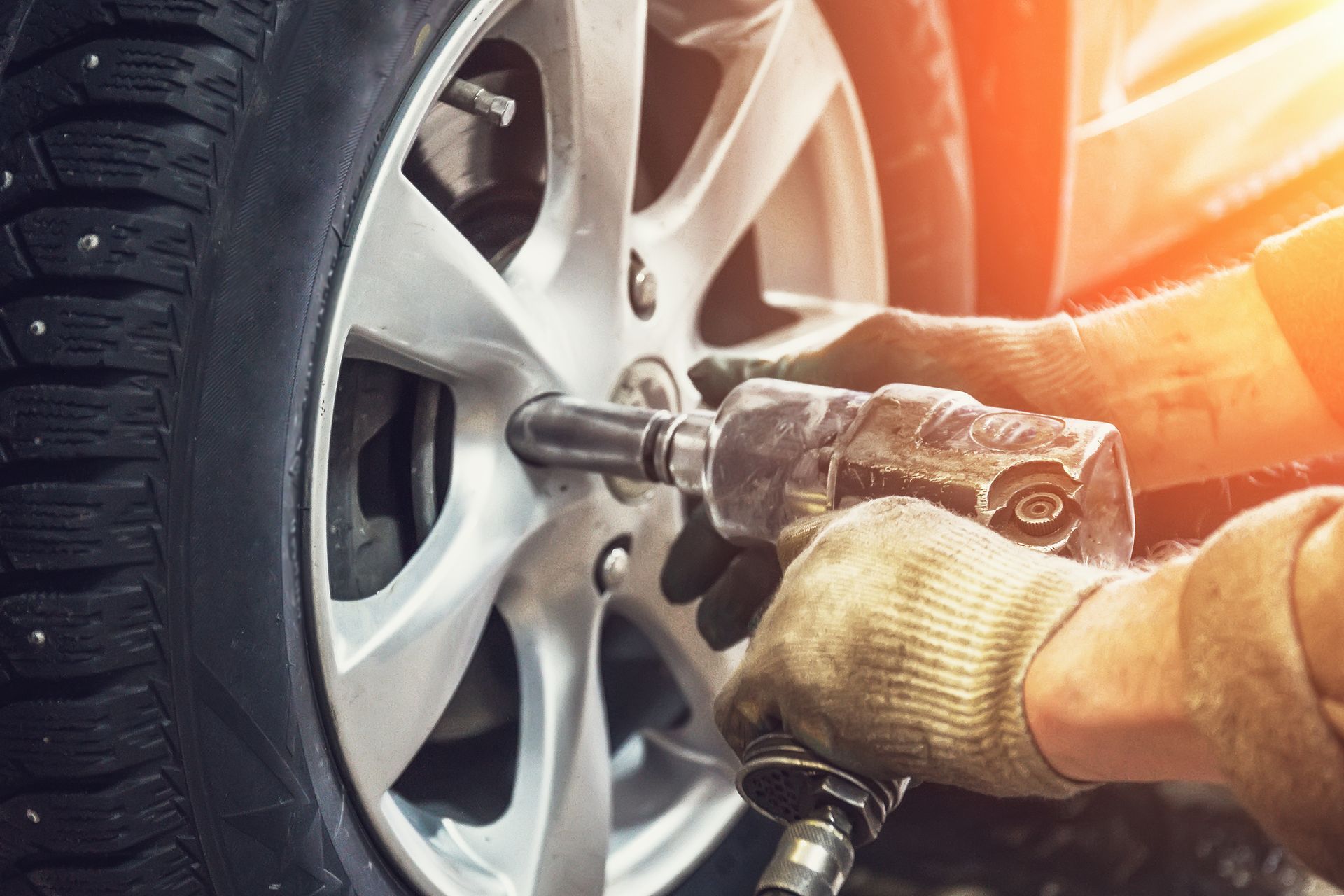 Mechanic using a pneumatic wrench to remove a lug nut from a car's tire. Mechanic using a pneumatic wrench to remove a lug nut from a car's tire.