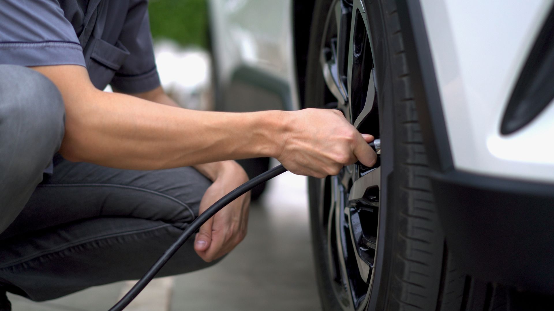 Person inflates a car tire with a black air hose. Person inflates a car tire with a black air hose.