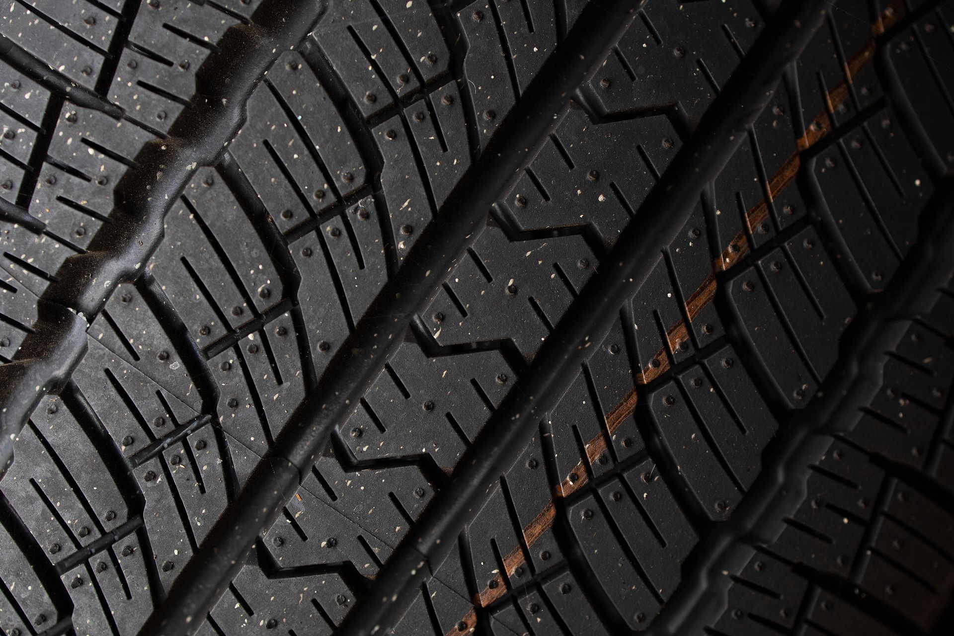 Close-up of a black tire tread with a deep pattern and small metal studs for enhanced grip.