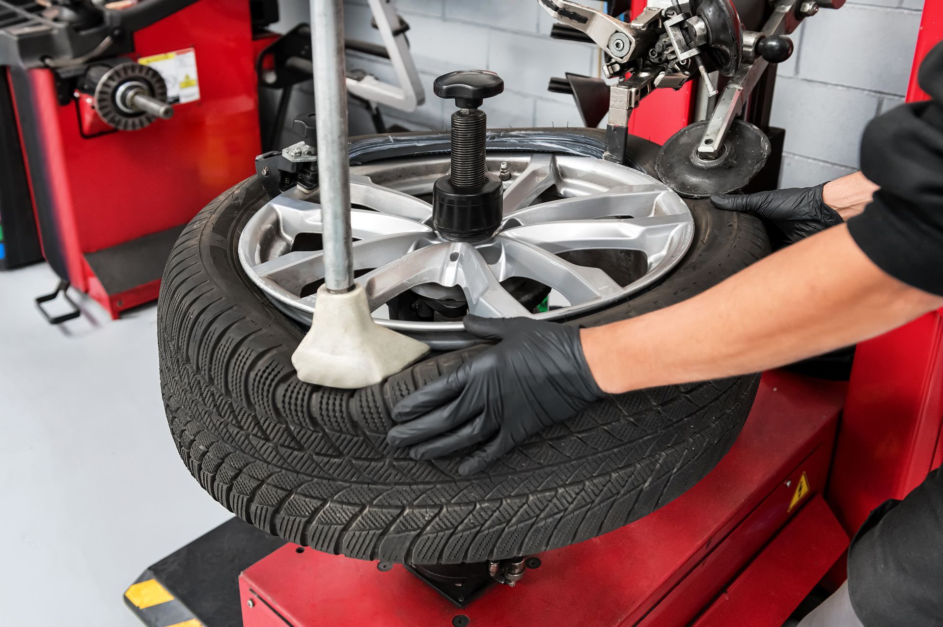Person in black gloves using tire machine to remove tire from rim.