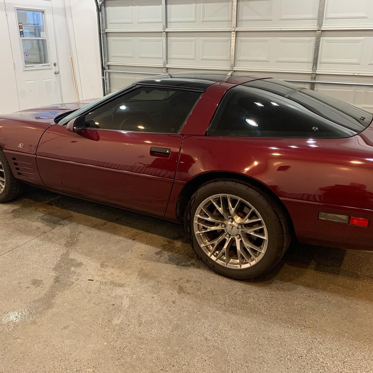 A red corvette is parked in a garage next to a garage door.