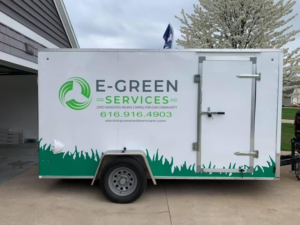 A trailer for e-green services is parked in front of a house