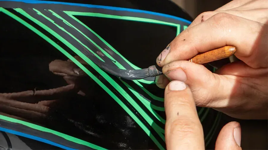 A person is painting a motorcycle with green and blue stripes